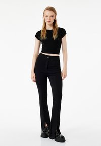 Schwarzes Crop-Top kombiniert mit hochgeschnittenen schwarzen Hosen mit seitlichen Schlitzen. Die Hosen haben ein elegantes Design und sind aus einem strukturierten Stoff gefertigt.