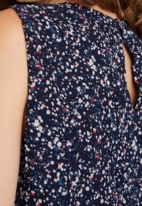 Navyfarbener Stoffoberteil mit einem mehrfarbigen gepunkteten Muster aus blauen, roten und weißen Punkten. Offenes Rückendesign mit einer Bindeschließe.