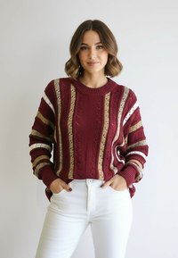 Bordowy sweter z dzianiny z kremowo-złotymi paskami, z okrągłym dekoltem i luźnymi rękawami. W zestawie z białymi jeansami.