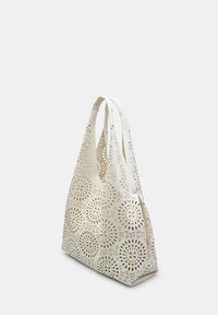 Hvid tote-taske med udskåret blomsterdesign, glat lædertekstur, lange håndtag og en rummelig, struktureret form.