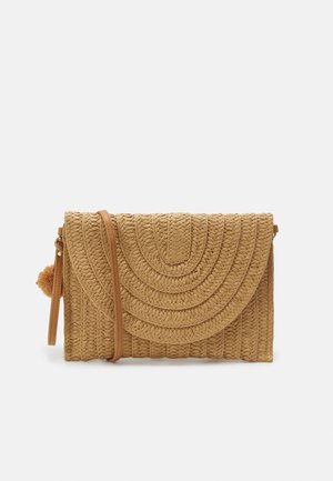 Tan flettet crossbody taske med klaplukning, buet syningsmønster, tynd rem og lille pompom fastgjort til lynlåstrækket.