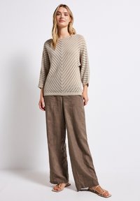 Beige knitted sweater with chevron pattern and three-quarter sleeves, paired with loose, light brown linen pants and flat sandals.