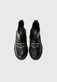 Bottines en cuir noir avec un bout arrondi, fermeture éclair, une boucle décorative en or et une semelle en caoutchouc texturée.