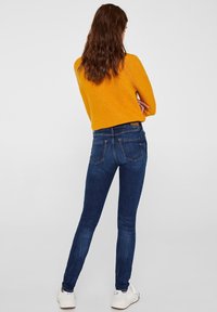 Dark blue skinny jeans with a smooth texture and rear pockets. Paired with a bright yellow loose-knit sweater, featuring long sleeves.
