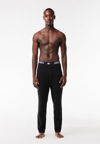 Schwarze Hosen aus weichem Stoff mit einem enganliegenden Bund und einem "LACOSTE"-Markenlogo. Das Design ist schlicht und figurbetont, ohne Muster.