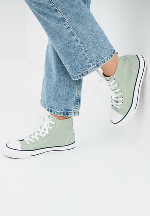 Baskets montantes en toile vert clair avec des lacets blancs, semelle en caoutchouc et détail de bande noire. Associées à un jean en denim bleu court.