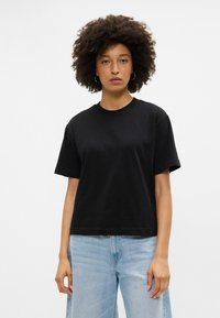 Juoda medvilninė marškinėliai su apvaliu kaklu ir trumpomis rankovėmis, su laisvu prigludimu. Suderinti su šviesiai mėlynomis plačiomis džinsomis.