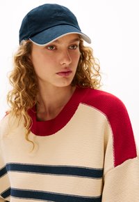 Marinehat med en kontrasterende hvid skygge, båret sammen med en creme- og rødstribet sweater med ribbet detaljering og tykk striktekstur.