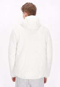 Witte pufferjas met capuchon, met een gequiltde textuur en gestikt patroon, weergegeven vanuit de achterkant. Grijze sweatpants zijn eronder zichtbaar.