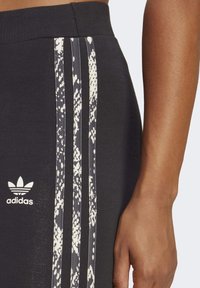 Svarta träningsbyxor med vitt Adidas-logotyp och tre prickiga vita ränder, visade på en persons midja och arm.