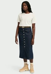 Saia de ganga de cintura alta, com fecho de botão na frente, duas bolsos de patch e costura em contraste. Combinada com uma t-shirt branca e botas beiges.
