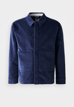 Giacca in velluto a coste blu navy con chiusura a bottoni, colletto a punta e due grandi tasche frontali. Tessuto liscio e vestibilità su misura.