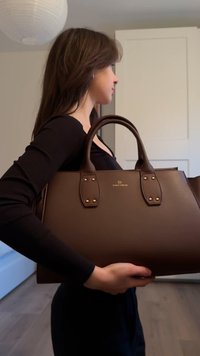 Borsa a mano in pelle marrone con due manici robusti, dettagli in metallo dorato, forma rettangolare, texture liscia e logo del marchio al centro.