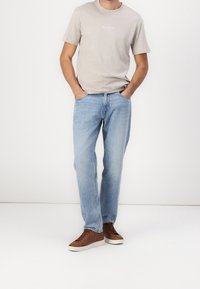 Světlé šedé tričko z bavlny s krátkými rukávy a nápisem na přední straně. Světle modré džínové kalhoty s volnějším střihem, doplněné o hnědé nízké tenisky.