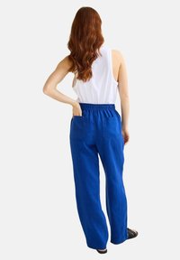 Pantalon large en lin bleu avec une taille élastique et deux poches arrière, associé à un débardeur blanc. Texture lisse et coupe décontractée.