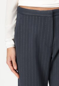 Navy pinstriped trousers with a smooth texture, featuring a flat waistband and side pockets, accented by thin white stripes.