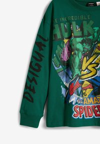 Grön bomullslångärmad skjorta med serietidningsgrafik av Hulk och Spider-Man, med "Desigual"-text i fet svart på ärmen.