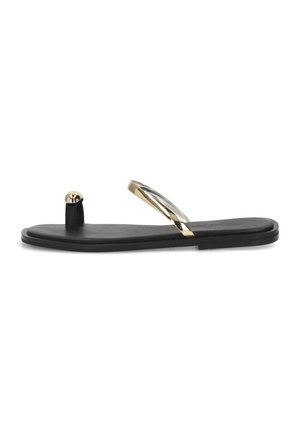 Sandal plana negra con aro dorado en el dedo y tira metálica dorada y transparente sobre el pie, sobre un fondo blanco.