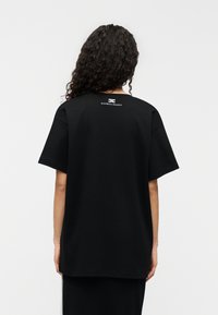 Μαύρο βαμβακερό υπερμεγέθες μπλουζάκι με κοντά μανίκια, με απλό στρογγυλό λαιμό και μικρό λευκό λογότυπο στο πίσω μέρος. Λεία υφή.