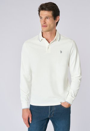Polo bianco a maniche lunghe con colletto e tre bottoni, caratterizzato da un sottile dettaglio di cucitura a contrasto e un piccolo logo sul petto.