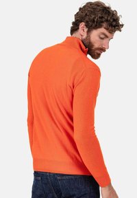 Pull-over orange avec col zippé et manches longues, fabriqué en tissu doux. Caractéristiques : poignets et ourlet côtelés, silhouette ajustée.