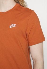 Oranžové bavlněné tričko s krátkým rukávem, na levém prsu s bílým logem Nike. Kolečkový výstřih a standardní střih.