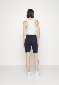 Lichtblauw crop tanktop en marineblauwe fietsbroek met witte zijsstripes. De outfit heeft een aansluitend ontwerp en een gladde stof.