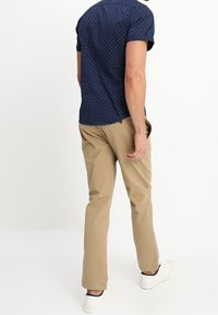 Camicia a maniche corte blu navy con pois bianchi, abbinata a pantaloni beige. L'outfit è completato da sneakers bianche. Design semplice e casual.