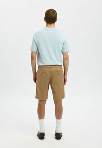 Svijetloplava polo majica, bež kratke hlače, bijele čarape, tamne cipele. Outfit sadrži klasični kroj i opušteni fit, s dugmadi na stražnjim džepovima.