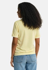 Unisex t-shirt met korte mouwen in lichtgeel katoen, met een ronde hals en contrasterende witte ribgebreide manchetten. Gemaakt met blauwe jeans.