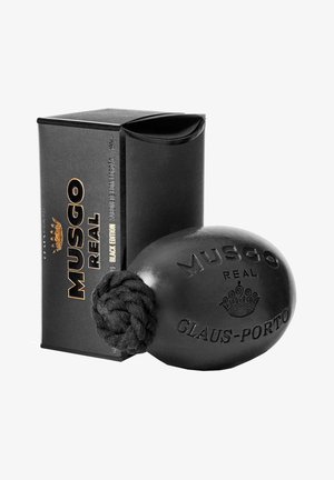 Zwarte scheerzeep in een ronde vorm, met een gevlochten touwhandvat, gegraveerd met de teksten "MUSGO REAL" en "GLAUS-PORTO". Zwarte doosverpakking.