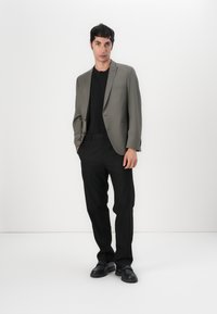 Blazer gris claro con solapas de muesca, camiseta negra y pantalones negros. Tela suave, corte entallado y zapatos de cuero negros.