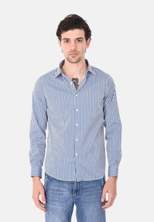 Camicia a righe blu e bianca con colletto, maniche lunghe e vestibilità slim. Indossata con jeans blu, che mostrano uno stile casual.