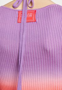 Lila Ombre-Oberteil mit gerippter Textur, ausgestattet mit einem roten Etikett mit der Aufschrift "VIGNE JEANS COUTURE" und einem Bindeband auf der Rückseite.