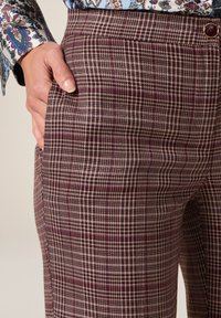 Pantalones de cuadros marrones con un corte ajustado, que presentan una textura suave, bolsillos laterales y un detalle de botón en la cinturilla.