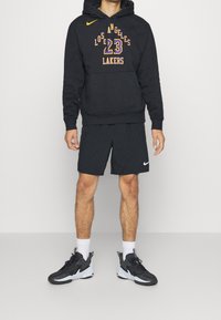 Haut à capuche noir avec "Los Angeles Lakers" et "23" en jaune, accompagné de shorts noirs. Chaussures de sport noires avec des accents blancs.