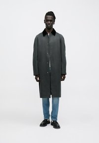 Pelēks mētelis ar melnu apkakli, pogu aizdari un sānu kabatām; kombinēts ar gaiši zilām džinsa biksēm un melniem apaviem stilīgam izskatam.