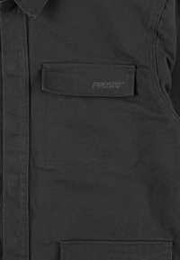 Czarna kamizelka z wyraźną kieszenią na piersi i teksturowaną powierzchnią. Posiada wytłoczone logo "PROSTO" na kieszeni.