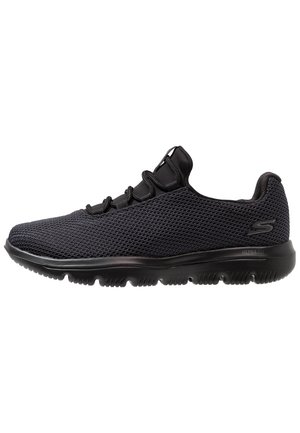Zapatilla deportiva negra Skechers con parte superior de tela de malla, cuello acolchado y suela de goma flexible con patrón antideslizante.