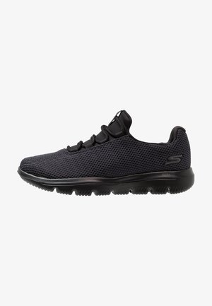 Zapatilla deportiva negra Skechers con parte superior de tela de malla, cuello acolchado y suela de goma flexible con patrón antideslizante.