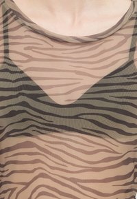 Caurspīdīgs sietiņš ar melniem un brūniem zebras svītrām atklāj zem tā atbilstošu svītrainu krūšturi.