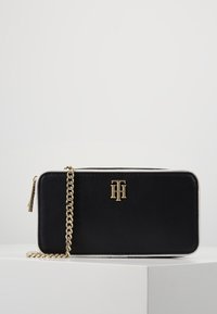 Black and white leather bag with a gold chain strap, featuring a gold logo on the front, rectangular shape, and smooth texture.