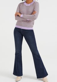 Randig tröja i rosa, svart och vitt, med en lila ribbad rundad halsringning och ärmslut, tillsammans med utsvängda mörkblå denimjeans.