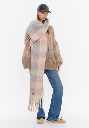 Overmaatse sjaal met een patroon in pastelkleuren, met franjeranden. Gekocht bij een losgebreid sweater en uitlopende jeans, met een pet.