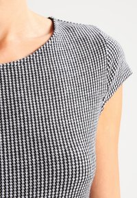 Sukienka w czarno-białą kratkę houndstooth z zaokrąglonym dekoltem i krótkimi rękawami, wykonana z teksturowanej tkaniny.