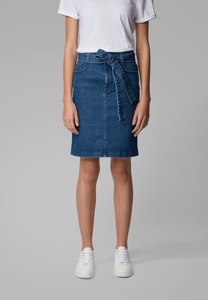 Spódnica dżinsowa w ciemnoniebieskim kolorze, o długości do kolan, związywana w talii materiałowym paskiem. Połączona z białym t-shirtem i białymi trampkami. Gładka tekstura.