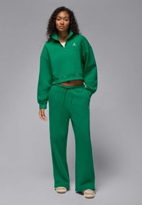 Zielona krótka bluza z wysokim kołnierzem i zamkiem, zestawiona z pasującymi dresami. Dresy mają talię ze sznurkiem i białe akcenty z logo.