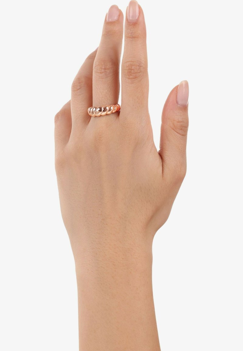 Anello in metallo rosa con un design intrecciato e bordi lisci e arrotondati. Posizionato su una mano con unghie naturali su uno sfondo bianco.