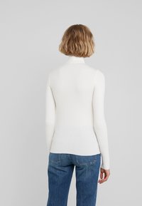 Vit ribbad långärmad topp med hög hals, åtsittande design och en slät textur, kombinerad med blå raka jeans.