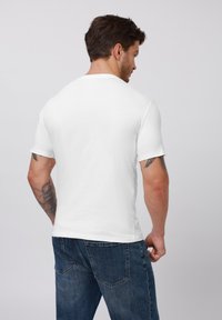 White short-sleeve t-shirt made of soft, smooth fabric, featuring a classic crew neck; worn with blue denim jeans, showcasing a casual fit.